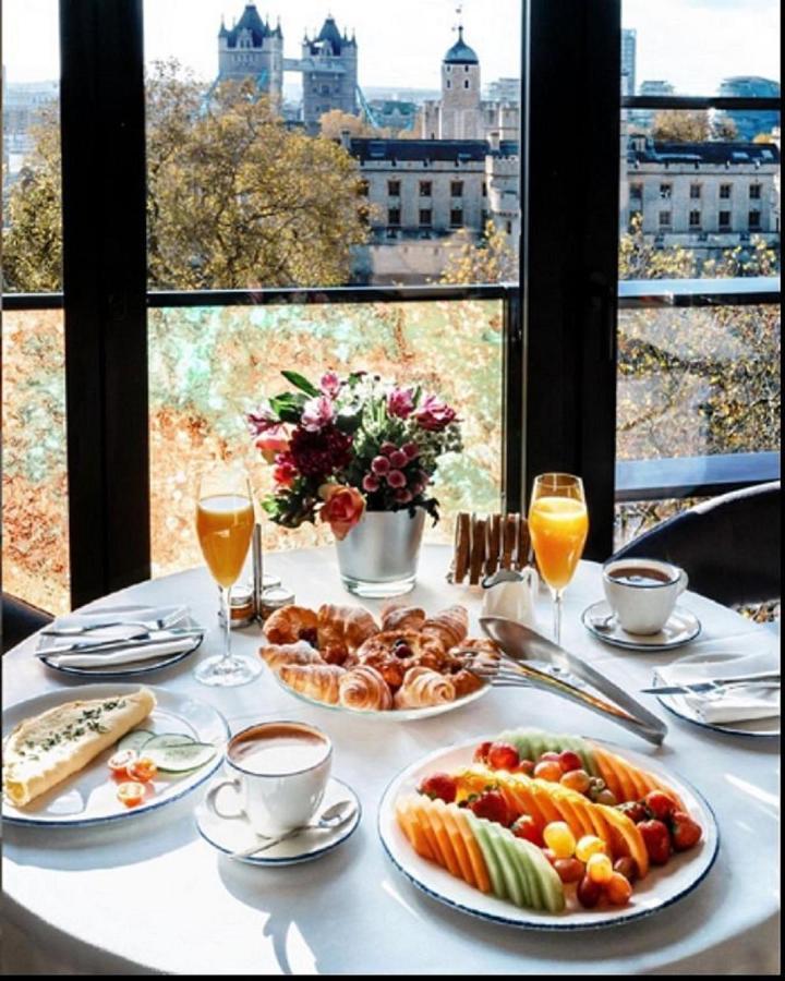Tower Suites By Blue Orchid Лондон Екстериор снимка The photo showcases a beautifully set breakfast table with a scenic view through large glass windows. The table features an array of items, including:

1. A small vase filled with colorful flowers.
2. Two glasses of orange juice.
3. A cup of coffee o
