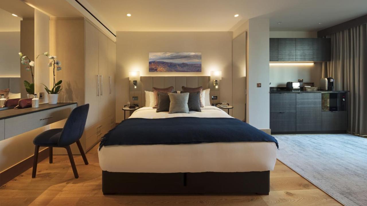 Tower Suites By Blue Orchid Лондон Екстериор снимка The photo displays a modern hotel room featuring a plush bed with a dark blue bedspread and several decorative pillows. The walls are adorned in neutral tones, and there is a piece of artwork above the bed depicting a serene landscape. On the side, t