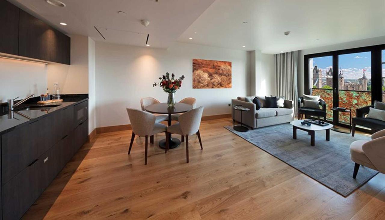 Tower Suites By Blue Orchid Лондон Екстериор снимка The photo shows a modern apartment interior. On the left side, there is a kitchen area with dark cabinetry, while on the right side, a comfortable living area is visible. In the center, a round dining table is set with four chairs and a vase of flowe