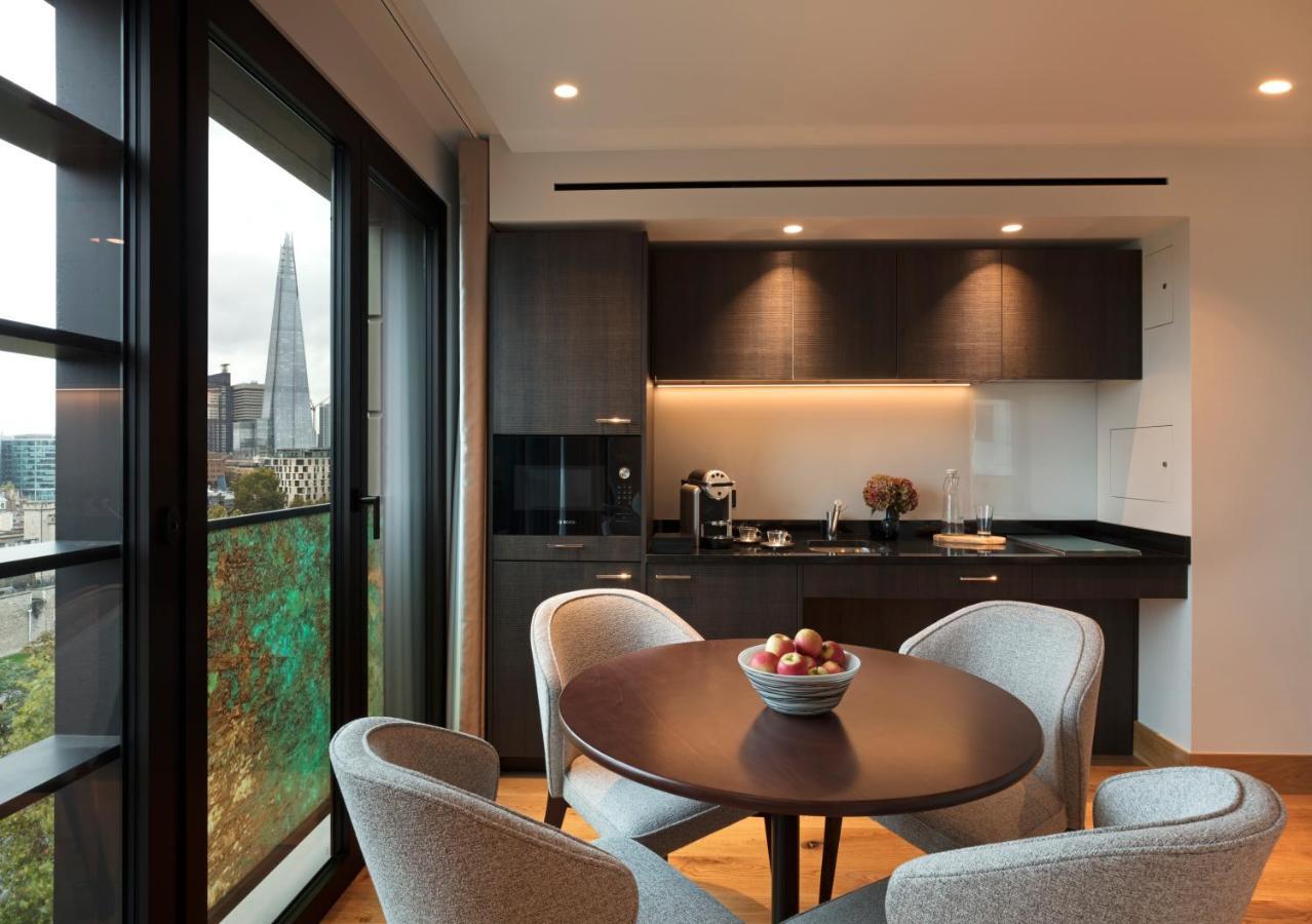 Tower Suites By Blue Orchid Лондон Екстериор снимка The photo shows a modern kitchen and dining area. It features a round table with four gray chairs, and a bowl of apples is placed in the center of the table. The kitchen has dark cabinetry, a black countertop, and built-in appliances. Large windows a