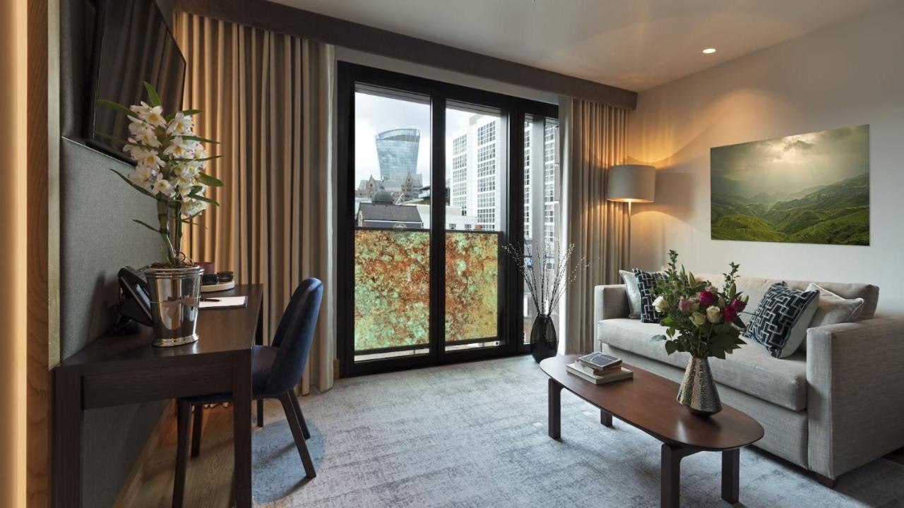 Tower Suites By Blue Orchid Лондон Екстериор снимка The photo shows a modern and well-lit living space. There is a comfortable sofa with decorative cushions, a small coffee table in front of it, and a floor lamp providing additional lighting. Beside the sofa, there are decorative plants and a vase wit