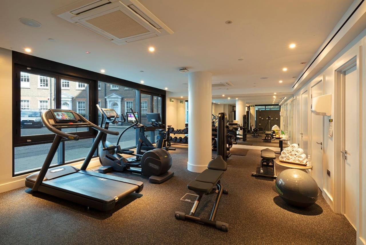 Tower Suites By Blue Orchid Лондон Екстериор снимка The photo shows a modern gym interior featuring various exercise equipment. On one side, there are several cardio machines, including treadmills and an elliptical. The gym has a spacious, bright feel with large windows allowing natural light to enter