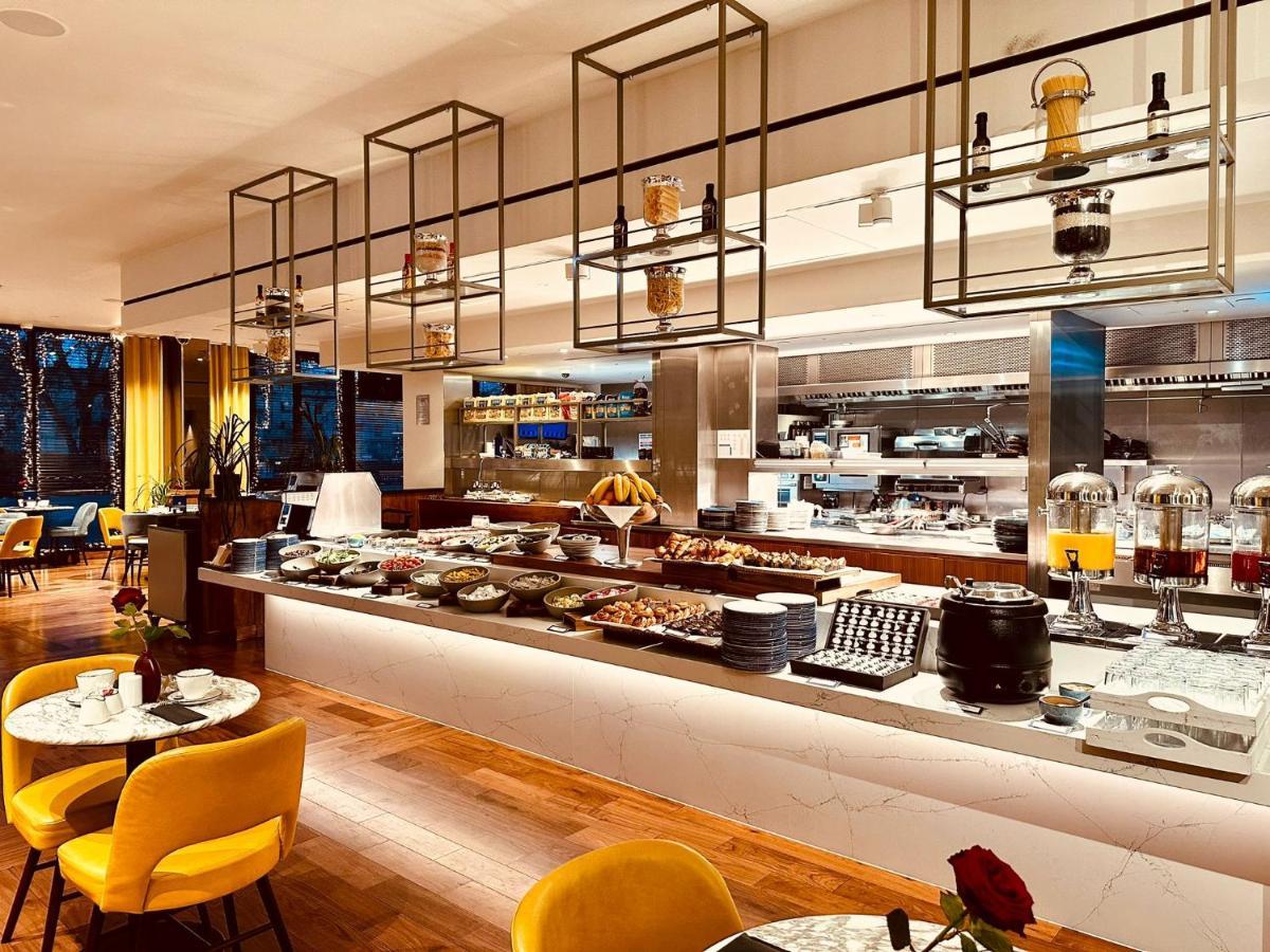 Tower Suites By Blue Orchid Лондон Екстериор снимка The photo shows a modern restaurant interior featuring a buffet layout. The space has a sleek design with wooden flooring and a bright, open atmosphere.  

The buffet counter is richly arranged with various dishes and food items, likely for a breakfa
